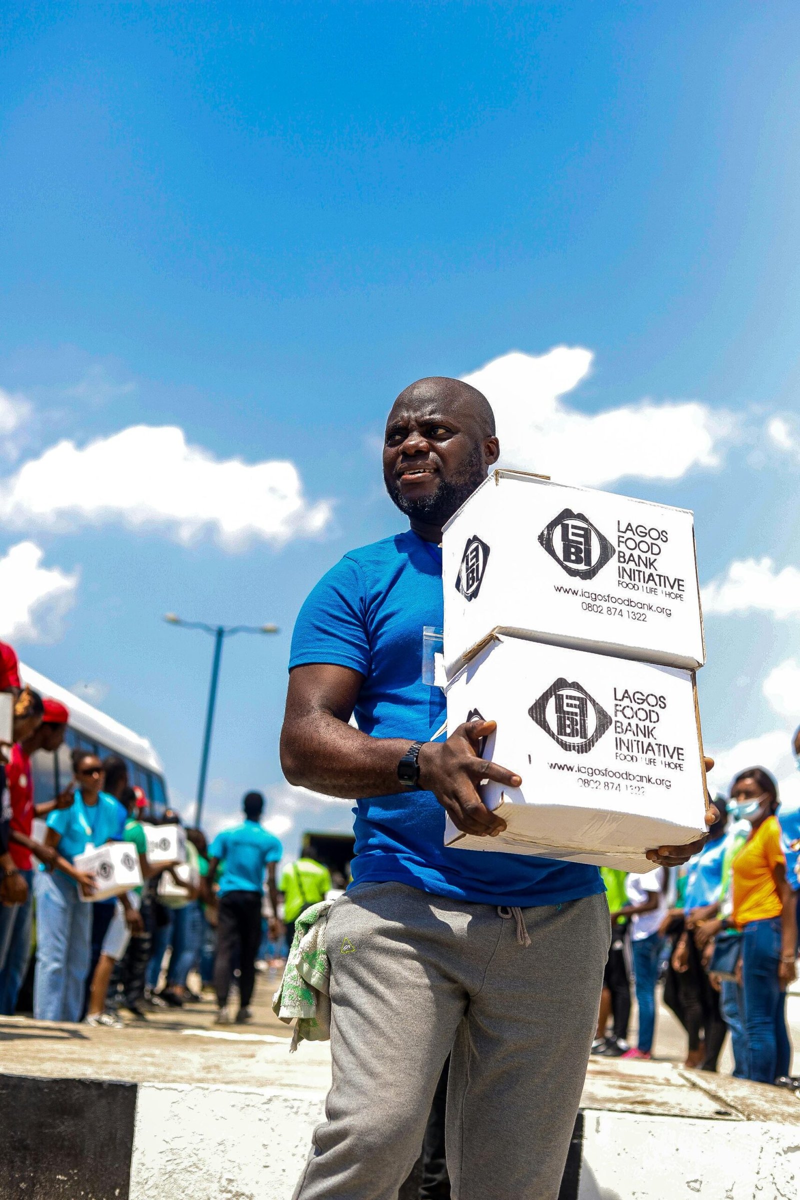 A man participates in food distribution for Lagos Food Bank Initiative under clear blue skies.